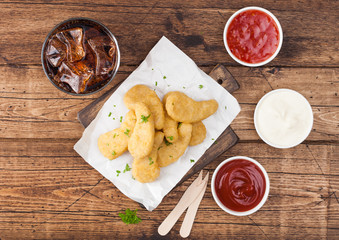 Buttered chicken nuggets on chopping board with glass of cola and ketchup on wooden background. Top view