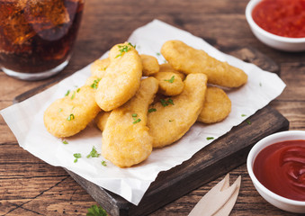 Buttered chicken nuggets on chopping board with glass of cola and ketchup on wooden background. Sour cream and sweet chilli sauce.