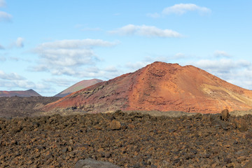 Volcanic landscape with lava field in the foreground and mountain range with different red and brown colours in the background on canary island Lanzarote