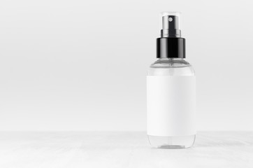 Transparent spray bottle for cosmetics product with white blank label on white wood board, mock up...