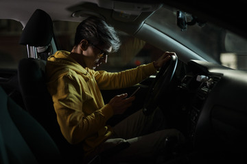 Driver man using smartphone in car phone holder at night