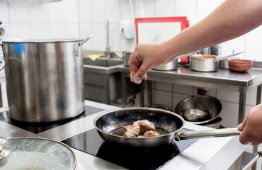 Chef cooks fried potatoes with pieces of meat in a restaurant kitchen