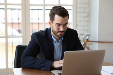 Confident businessman wearing glasses working on laptop in modern office