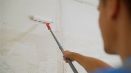 Worker in a blue suit is processing the wall. Worker plastering a wall. Worker with a roller