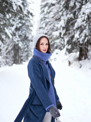 Obraz premium brunette walks through the winter forest in a gray hat, blue sweater and blue coat.
