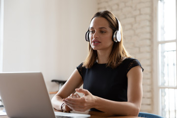 Focused businesswoman wearing headset looking at laptop screen and talking