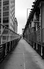 West-bound view along the Manhattan Bridge pedestrian walkway, leading from Brooklyn toward Manhattan, New York City, NY. Black and white image and vanishing point.