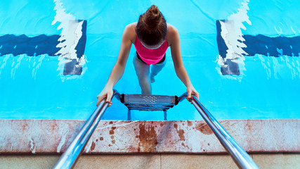 Young healthy athlete fitness swimmer female in swimsuit using pool ladder during swimming in sports pool in leisure centre