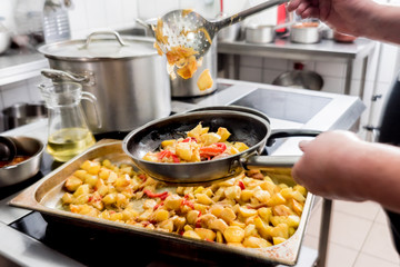 Chef cooks fried potatoes with pieces of meat in a restaurant kitchen