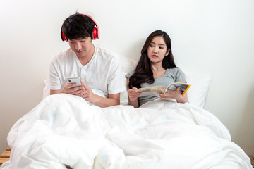 Obraz premium Young Asian wife looking at the phone screen of her husband on white bed in bedroom