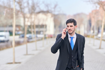 elegant young businessman talking on his cell phone in a clean, unfocused outdoor background