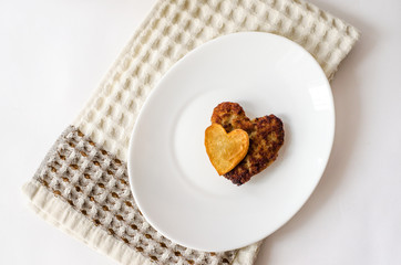 Fried cutlet in the shape of a heart, on it lies a heart of fried potatoes on a white oval plate. A gift for a loved one. Close up. Selective focus