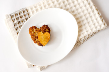 Fried cutlet in the shape of a heart, on it lies a heart of fried potatoes on a white oval plate. A gift for a loved one. Close up. Selective focus