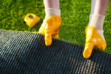 Greenering with the green artificial grass background. Worker holds a roll of green artificial turf.