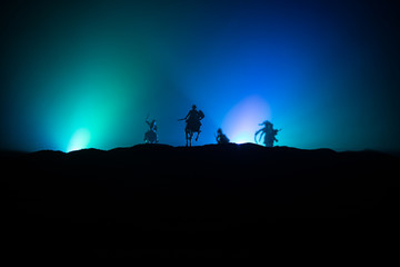 Medieval battle scene with cavalry and infantry. Silhouettes of figures as separate objects, fight between warriors on dark toned foggy background. Night scene.