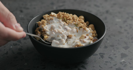 man hand eat whole grain granola with hazelnuts and pumpkin seeds in black bowl on terrazzo countertop