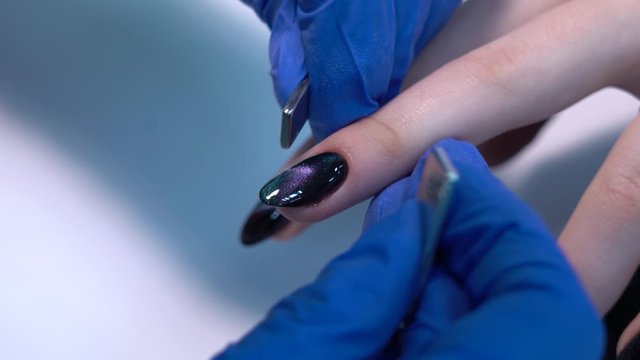 Closeup view of hands of professional manicurist doing modern trendy holiday naildesign using magnets and special glossy sparkling gel polish with shiny cat eye effect. 4k video footage.