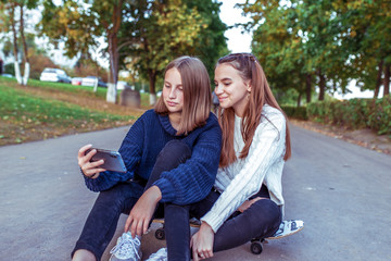 Fototapeta premium 2 girls schoolgirls teenagers 13-15 years old, autumn day, summer in city, holding smartphone, happy laughing joyful smiling. The best girlfriends watch videos in application online Internet.