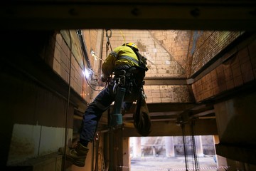 Industrial rope access abseiler welder wearing safety harness, abseiling commencing welding repairing at construction site, Perth, Australia 