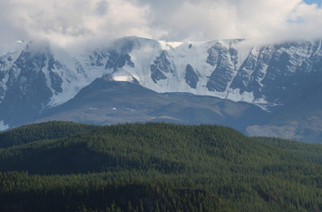 Mountain landscape, snow-capped peaks and forested hills. Summer evening, cloudy sky.