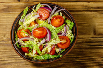 Healthy salad with savoy cabbage, cherry tomato, red onion and olive oil on wooden table. Top view