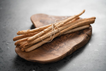 bunch of handmade wholegrain grissini tied with rope on olive board