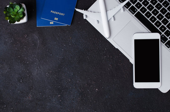 Travel booking concept. Laptop, passports, smartphone and airplane model on dark background.