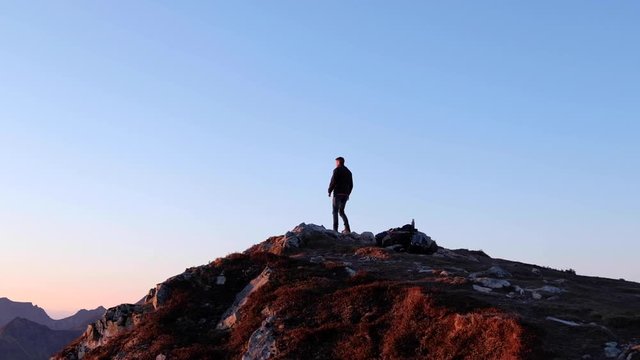 Hiker is climbing a mountain peak at the Lofoten Islands at Sunset in Slow Motion.