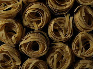 Uncooked tagliatelle pasta noodles isolated on black background and texture