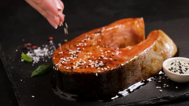 Slow motion of season teriyaki salmon with sesame seeds on a black slate background. Asian cuisine cooking food