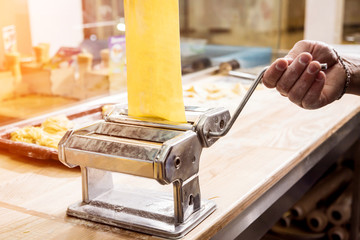 Chef rolling dough with a pasta machine. Pasta maker machine. Homemade italian style cuisine. Restaurant.