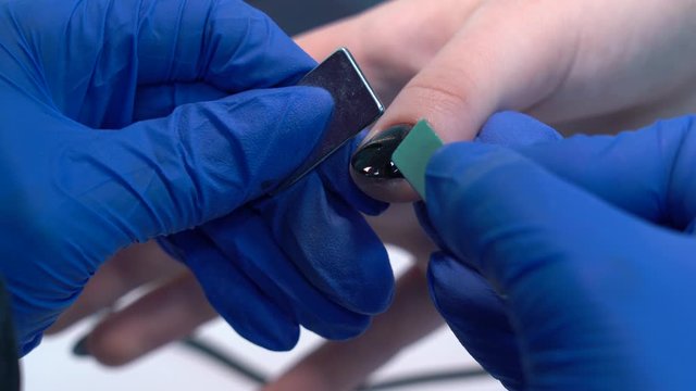 Closeup view of hands of professional manicurist doing modern trendy holiday naildesign using magnets and special glossy sparkling gel polish with shiny cat eye effect. 4k video footage.