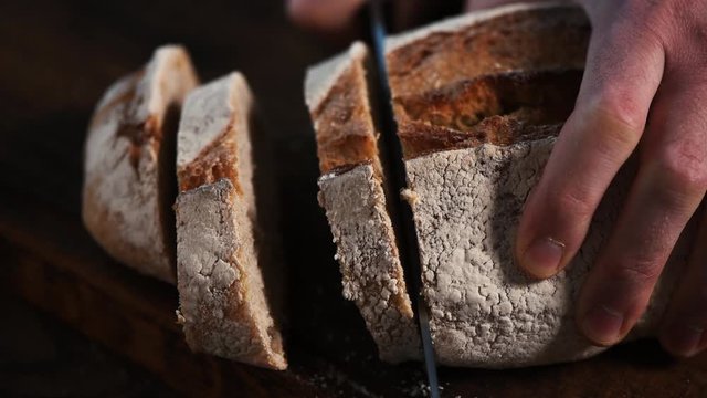 Slicing sourdough white bread on a dark wooden background. Slow motion of cutting bread with a knife