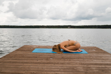 Fit slim woman practicing yoga exercises wearing mini swimsuit bikini at lake with clouds - Yoga meditation and wellness lifestyle concept - European Eastern Latvia Riga