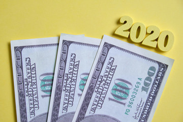 The concept of new investments in 2020. Dollars next to wooden figures on a yellow background. Top...