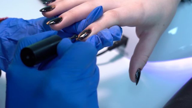 Closeup view of beautiful manicured nails of woman and professional manicurist applying transparent finish top polish laer of gel polish. Black design with shiny sparkling cat eye effect. 4k video