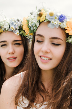 sisters with flowercrowns in fieldclose up portrait of two natural hippie girls with flowers in hair sitting on a green field