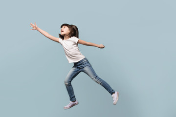 Fototapeta na wymiar Happy little preschool girl jumping on blue background.