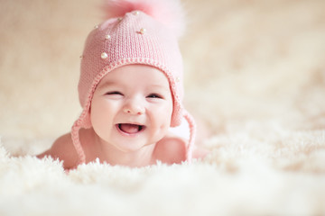 Laughing baby under 1 year old wearing knitted pink hat lying in bed closeup. Looking at camera....