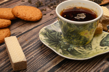 A Cup of black tea, tea leaves, pieces of brown sugar, oatmeal cookies, waffles on a wooden background. Close up.