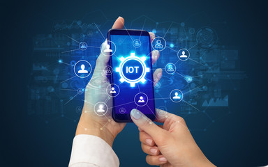 Female hand holding smartphone with IOT abbreviation, modern technology concept