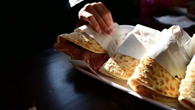 Small overview of a tray of piadine from Romagna (Italy). It is possible to see the filling of ham and cheese on the side. Selective focus on the casings. A hand grabs one.