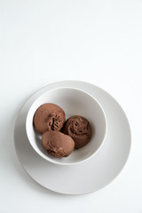 Three brown sponge cakes lie in a deep white plate. It stands on another flat, white plate. Flat lay, vertical composition on a white background with copy space.