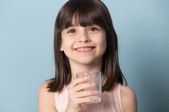 Smiling preschool cutie holding glass organic milk or yoghurt.