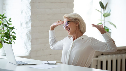 Aged businesswoman relaxing on chair stretching arms enjoy workday ends