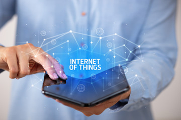 Businessman holding a foldable smartphone with INTERNET OF THINGS inscription, new technology concept