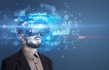 Businessman looking through Virtual Reality glasses with VIRTUAL inscription, innovative technology concept