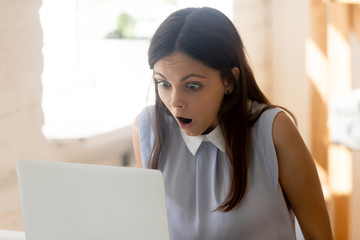 Businesswoman makes big eyes looking at computer screen feels shocked
