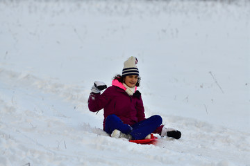 Fototapeta na wymiar Girl sledding downhill on snow in winter and laughing with joy