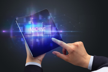 Obraz na płótnie Canvas Businessman holding a foldable smartphone with MACHINE inscription, new technology concept